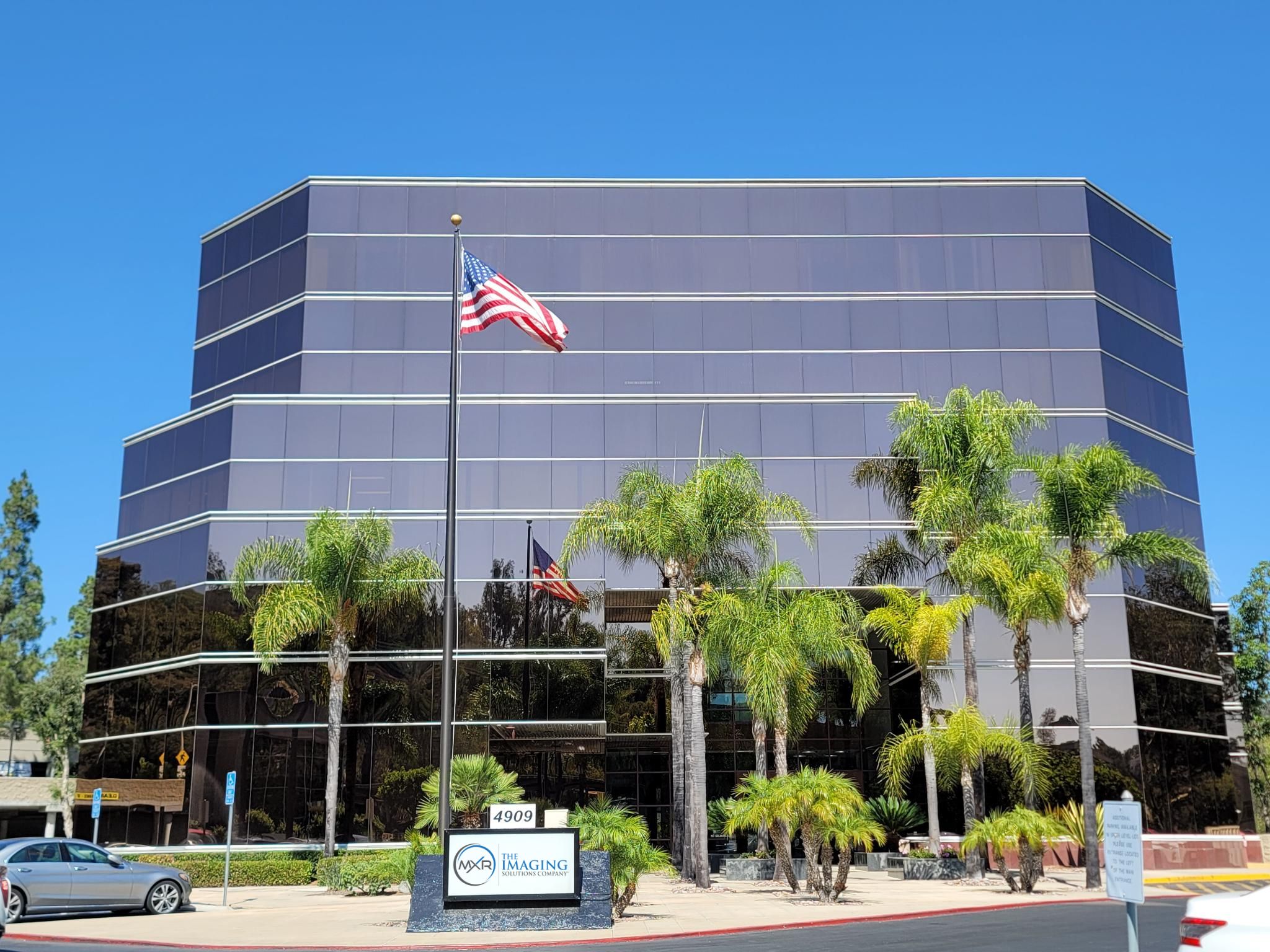 Exterior of the MXR Imaging corporate office, with prominent signage, palm tree landscaping, and a blue sky.